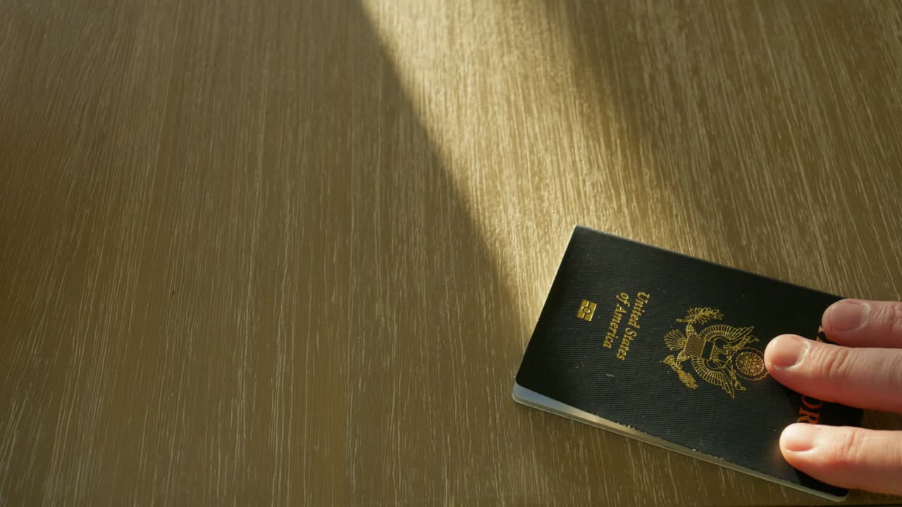 Starší mužská ruka podává venezuelský pas, druhá ruka pas bere a vrací mu pas Spojených států.