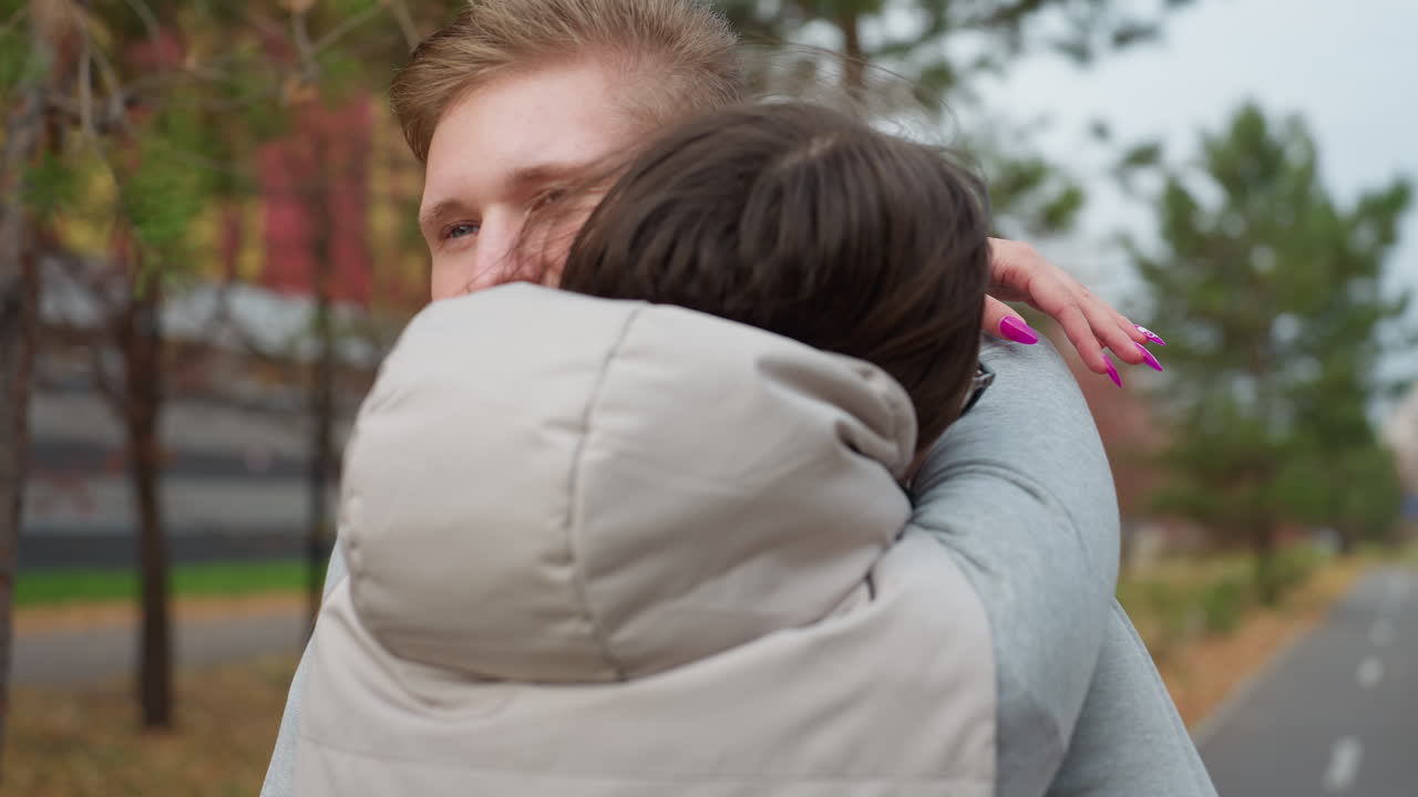 Close up back view of woman walking toward friend for warm embrace on peaceful autumn day with colorful trees, soft breeze blowing, and friend smiling with eyes closed waiting on park pathway