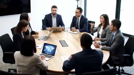 collaborative business meeting featuring diverse professionals engaged in discussion with laptops and presentations in a modern conference room