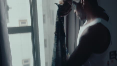 black man putting on shirt by the window at home