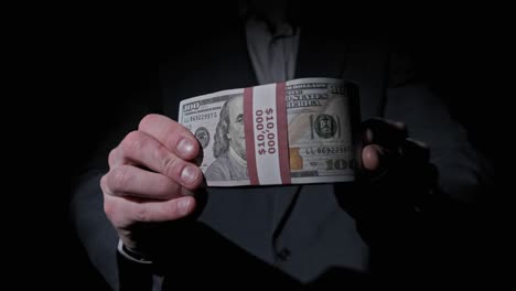 businessman in suit shows stack of 10000 american dollars on black background