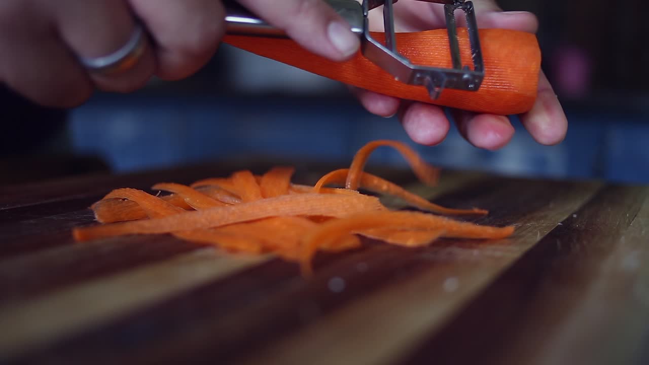 Primo piano: pelapatate utilizzato per sbucciare una carota arancione nella preparazione del cibo.
