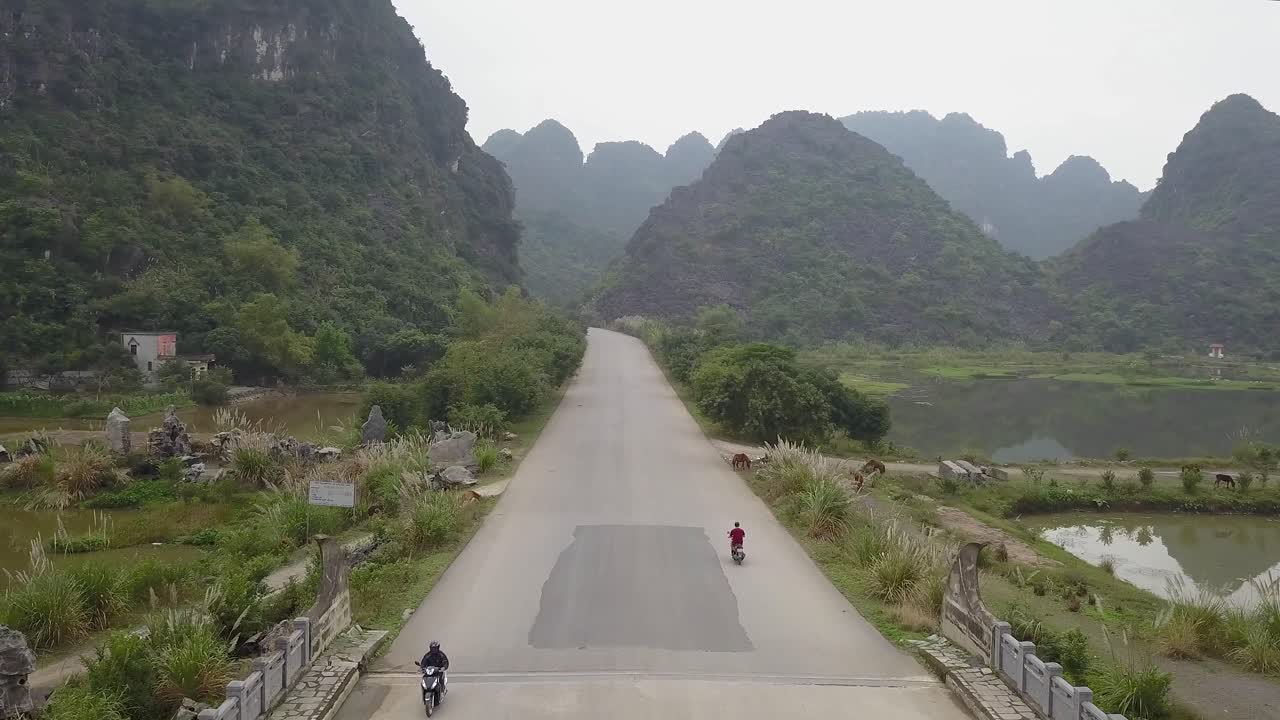 Fly over drone cam of red shirt motorbiker, oncoming traffic and big limestone mountains