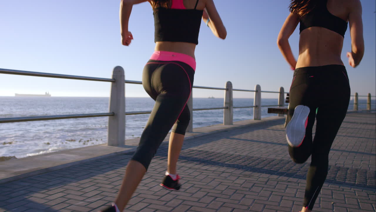 dos mujeres atléticas corriendo al aire libre en cámara lenta en el paseo marítimo al atardecer cerca del océano disfrutando de la carrera nocturna
