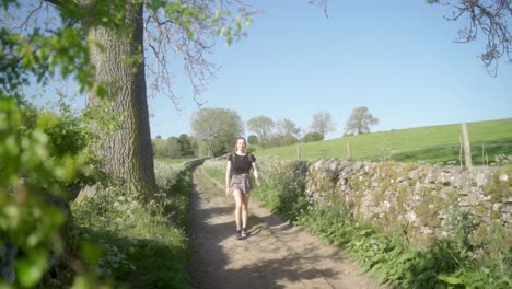 Slow-mo-of-blonde-woman-smiling-walking-towards-camera-along-dirt-track-Ashbourne,-Peak-District,-England