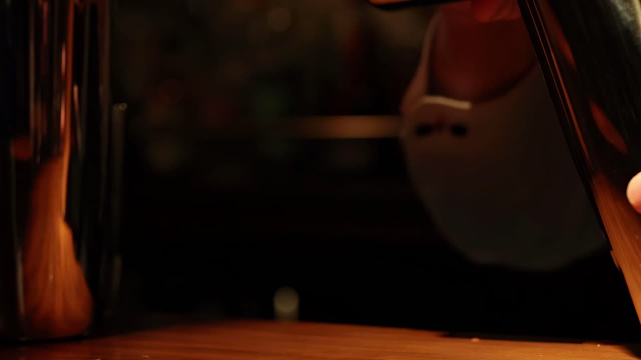 Close-up sequence of hands holding and maneuvering a reflective cocktail shaker on a wooden bar counter.