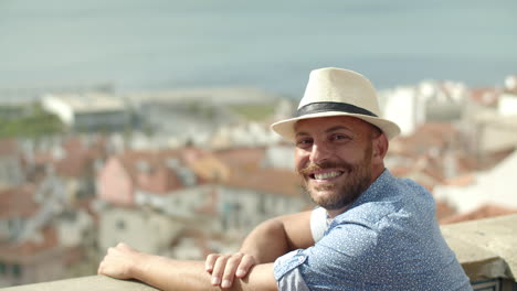 cámara lenta de hombre feliz con sombrero blanco mirando el paisaje urbano desde el punto de vista y luego, mira a la cámara y sonríe