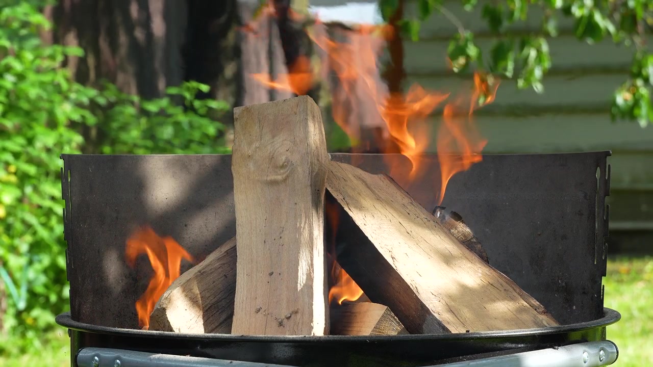 Nahaufnahme in Zeitlupe von brennendem Brennholz in einem Holzkohlegrill mit aufsteigenden Flammen und Rauch