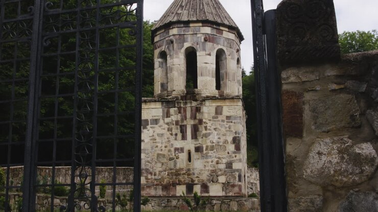 Cancello in ferro battuto aperto, torre in pietra del monastero di Mtsvane sullo sfondo.