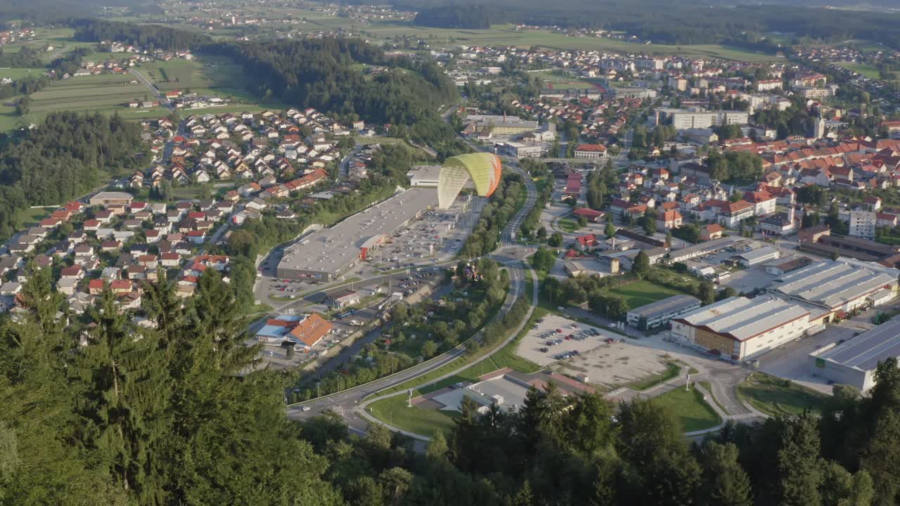 Aerial View Of Paraglider Soaring Above Town In Slovenia. Follow Shot