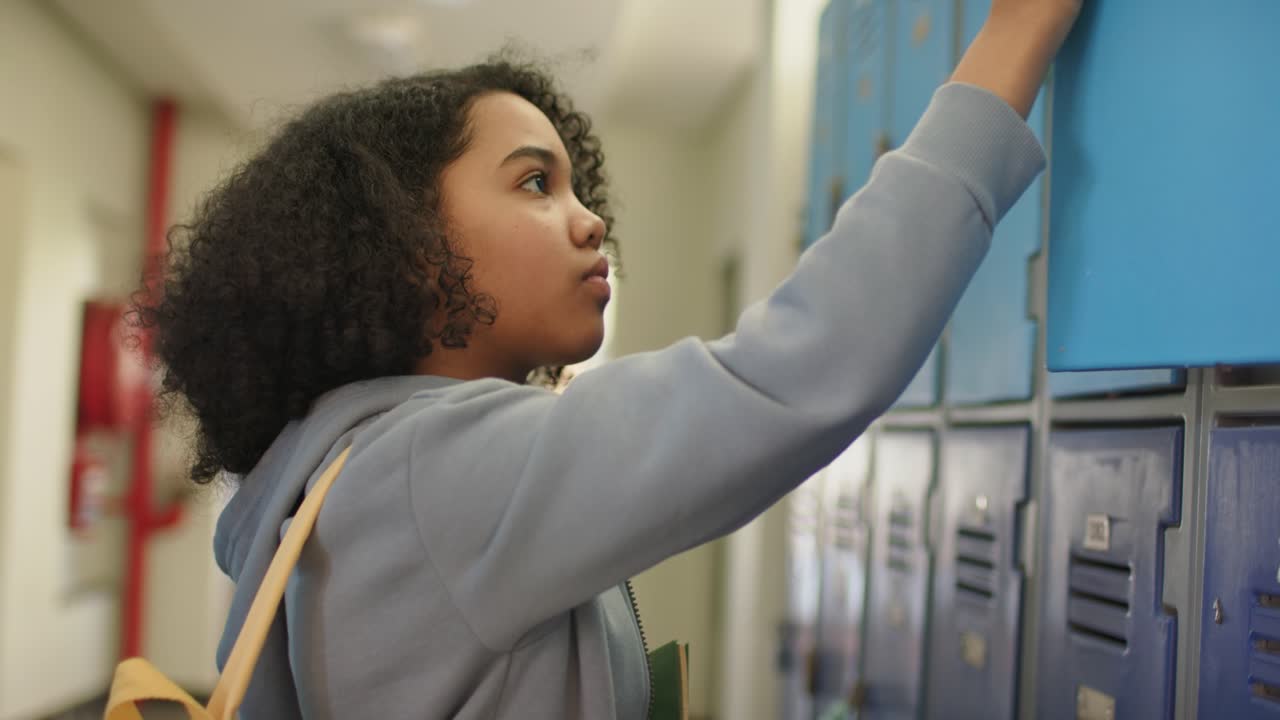 Adolescente afroamericano apre un armadietto blu, prende una cartella e sistema lo spallaccio di uno zaino giallo per la lezione.