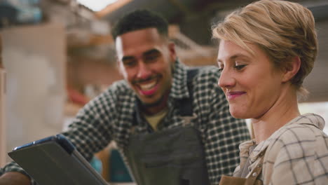 aprendices masculinos y femeninos con tabletas digitales trabajando como carpinteros en un taller de muebles