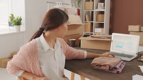 mujer sentada frente a la computadora que administra la tienda en línea, mira la cámara con una cara seria