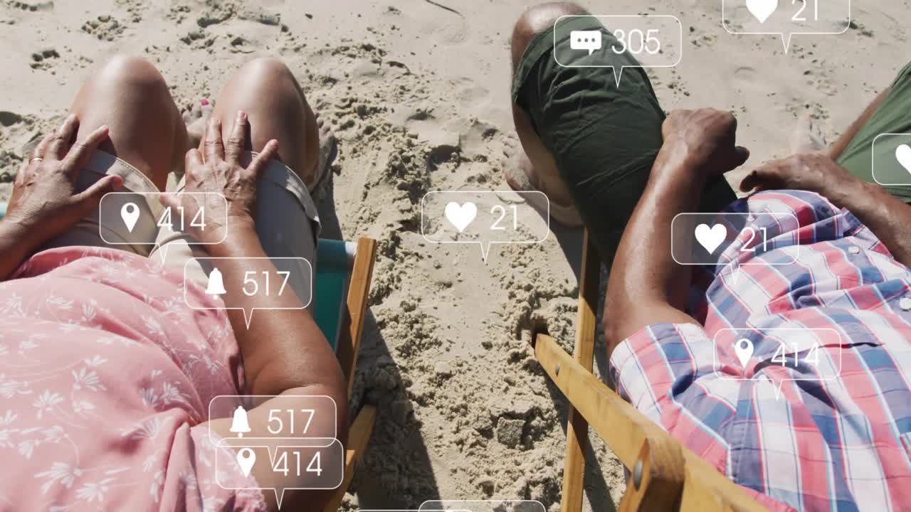 Älteres Paar entspannt auf Liegestühlen im Sand, betrachtet schwebende Engagement-Icons auf ihrem Höhepunkt und hält Händchen.