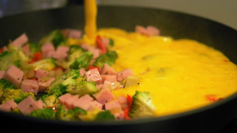 Pouring-mixed-eggs-into-a-hot-pan-with-vegetables,-making-a-fresh-and-healthy-omelet---Slowmotion