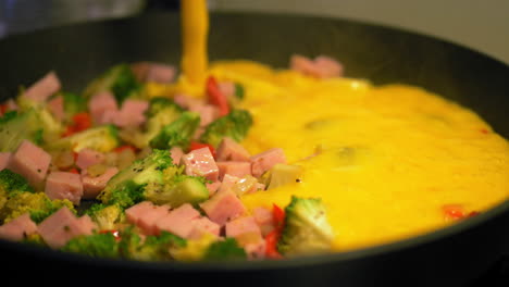 vertiendo huevos mixtos en una sartén caliente con verduras, haciendo una tortilla fresca y saludable - cámara lenta