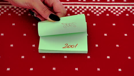 adult hand flipping through post-it notes with change of year against red design background