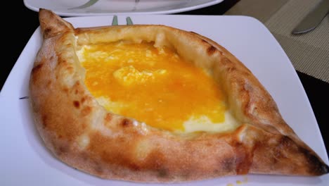 adjarian khachapuri en una mesa en un restaurante georgiano. pastel de pan abierto con yema de huevo