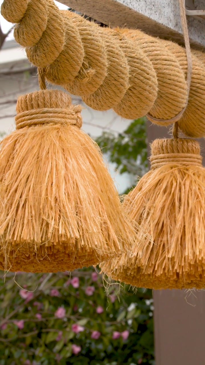 Primo piano di una tradizionale corda shimenawa di paglia e nappe appese a un torii di pietra.