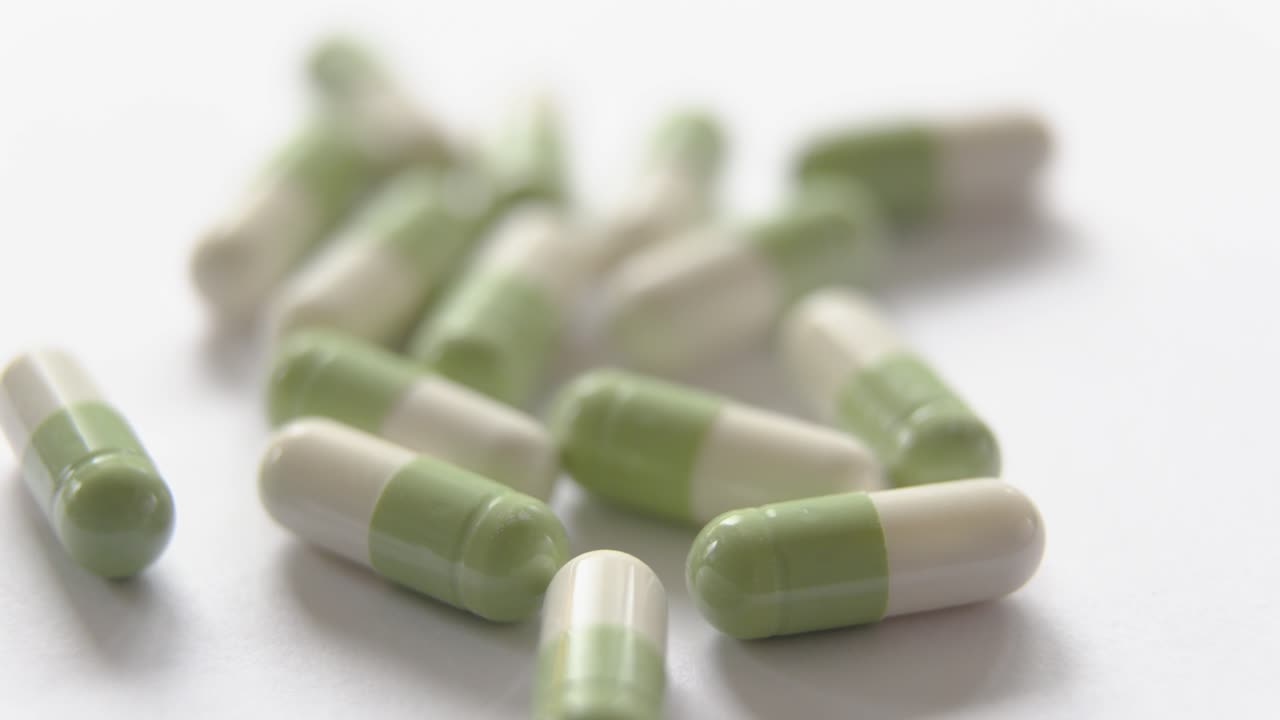 sideways shot from left to right of several white and green capsules on a white lighted surface