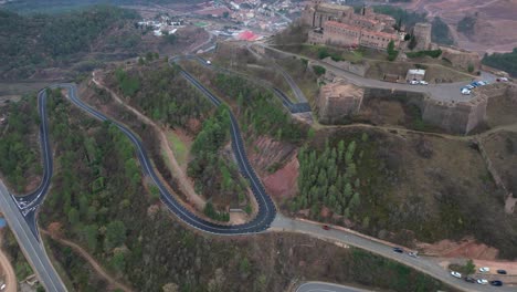 Winding-roads-leading-up-to-cardona-castle-surrounded-by-lush-greenery,-aerial-view