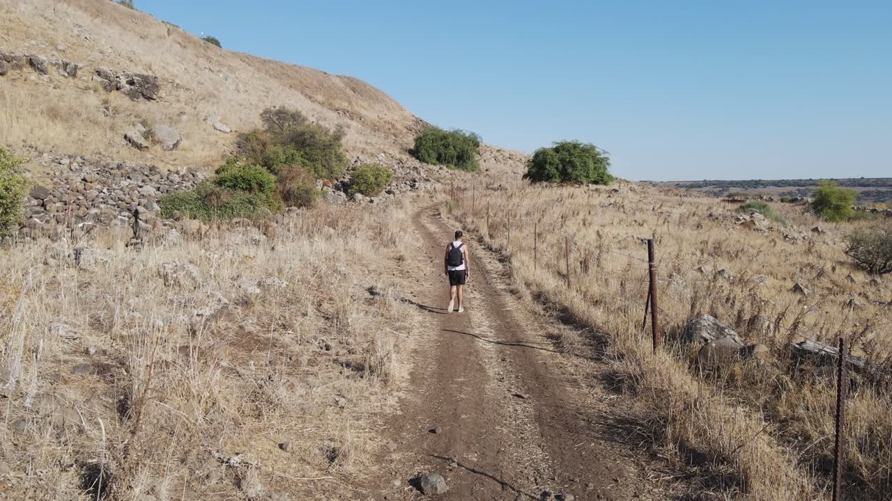 Un escursionista che cammina da solo lungo una strada sterrata in un paesaggio arido e collinare in Israele, nelle Alture del Golan.