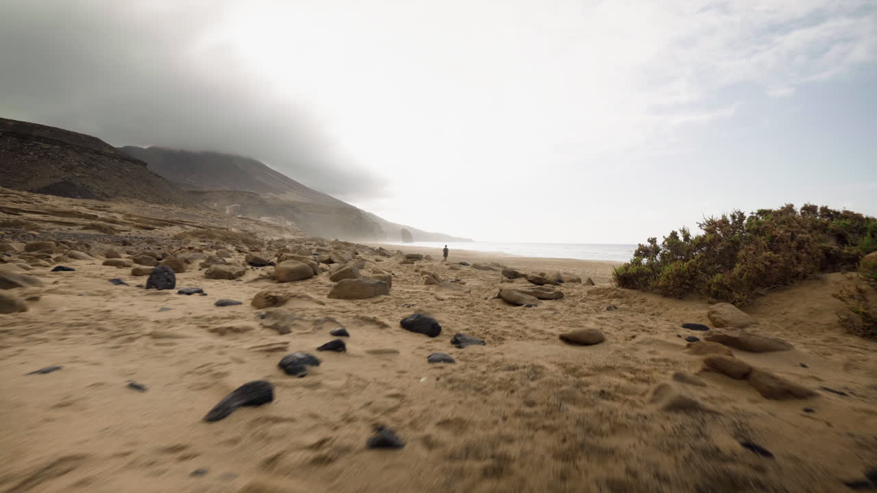 Fuerteventura island, canary Spain, walking fast on sand beach with lonely woman standing alone at distance nearby the ocean water