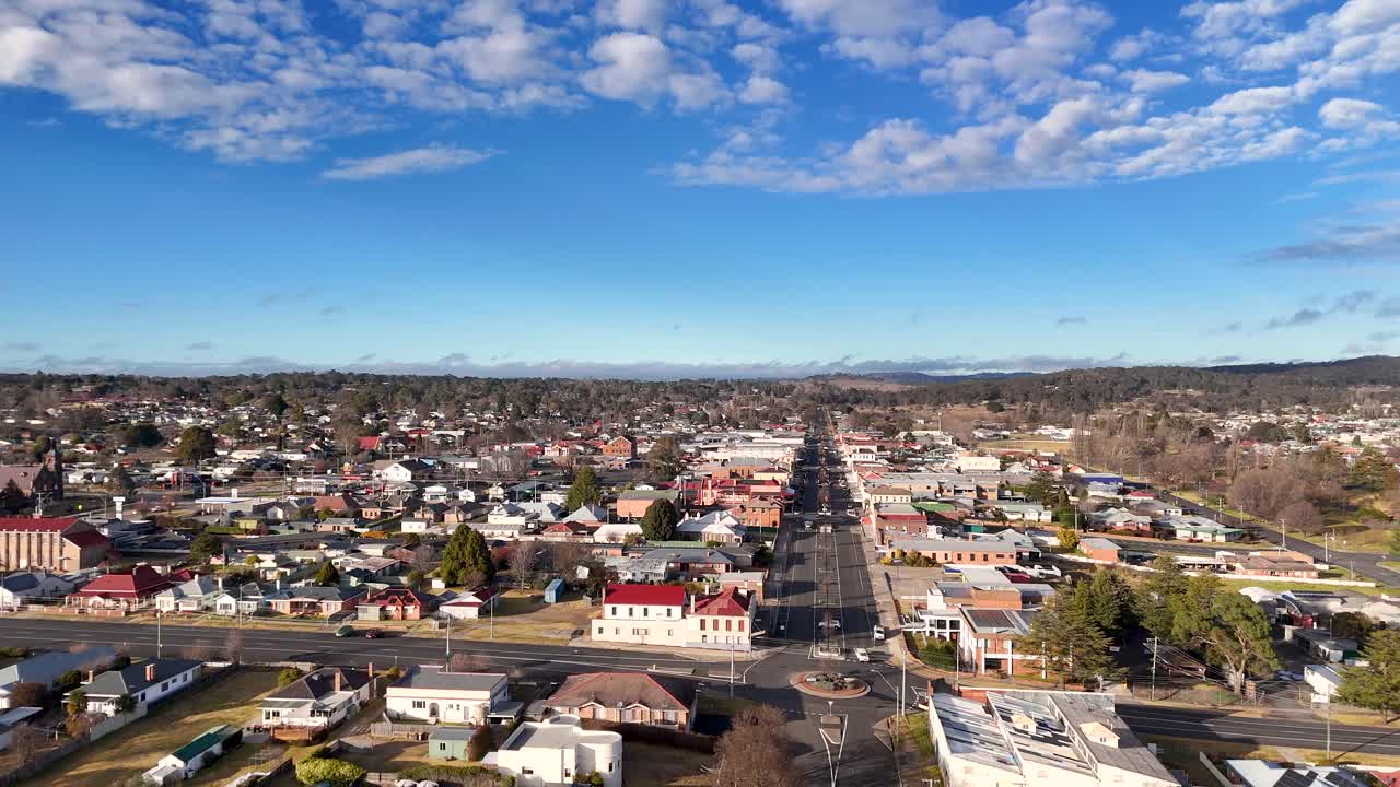 Aerial footage moves steadily above a residential main street in Glen Innes, Australia, under bright daylight with scattered clouds and clear urban layout