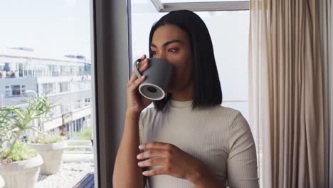 Mixed-race-gender-fluid-person-drinking-a-cup-of-coffee-and-looking-through-window