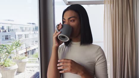 mixed race gender fluid person drinking a cup of coffee and looking through window