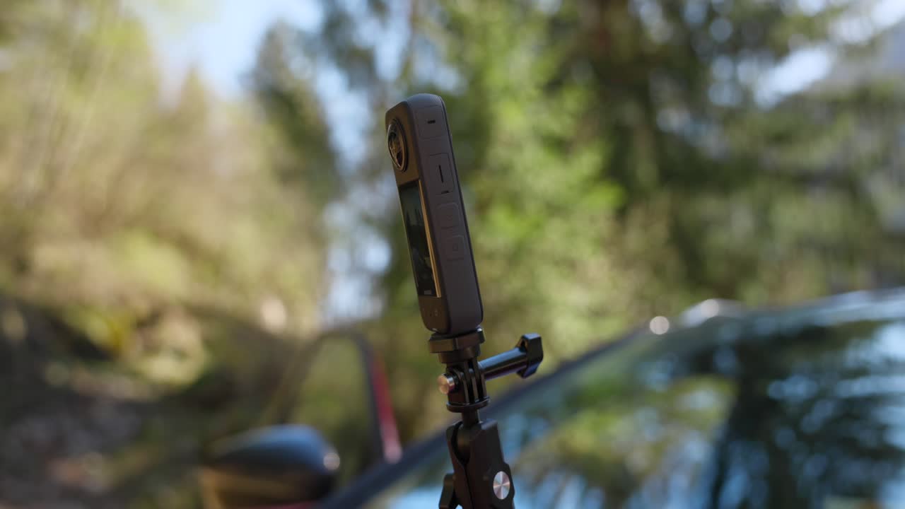 인스타360x3 액션 카메라가 자연 배경에서 차에 서 있습니다.