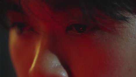 close-up of a human eye reflecting red light in a dark, dramatic setting