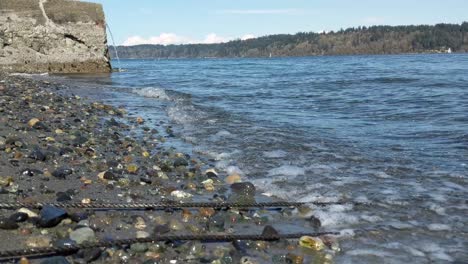 small waves lapping on a sand and pebble beach with a sea wal in the back ground