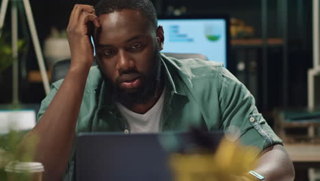 closeup disappointed afro business man talking via laptop in night office