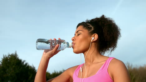 fit woman drinking water after jogging outside