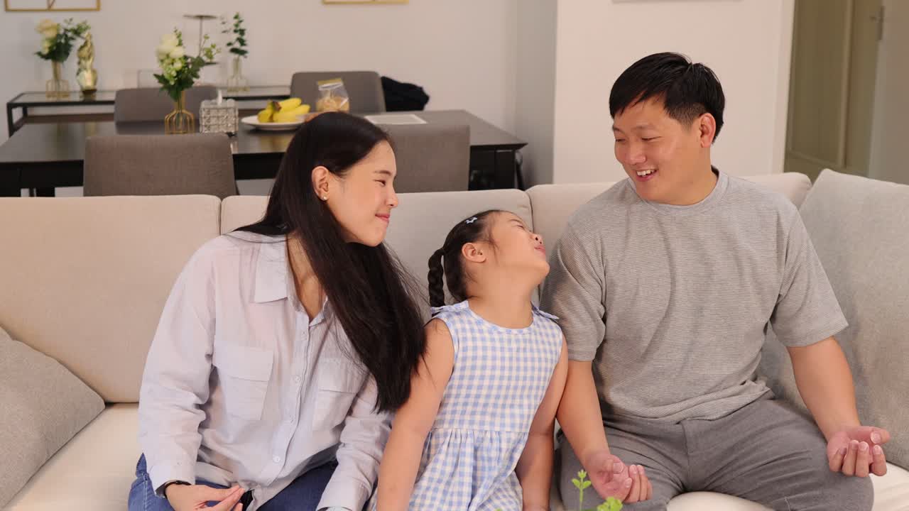 A family of three enjoys a peaceful meditation session on a sofa in a warmly lit living room