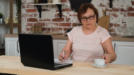 mujer mayor que utiliza una computadora portátil para trabajar a distancia en casa