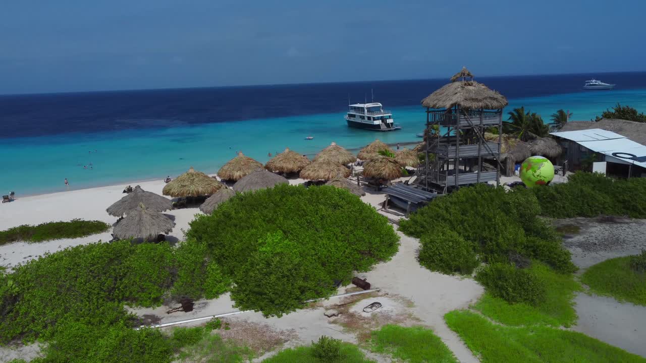 Aerial around watch tower overlooking beach palapas, boat, yacht in turquoise water