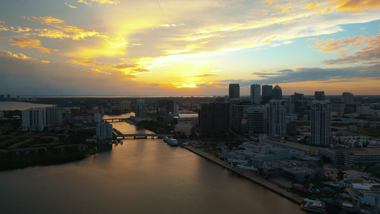 High above establishing shot of the Tampa skyline at sunset, with light shimmering on the Ybor basin waterway. Aerial tracking to the right