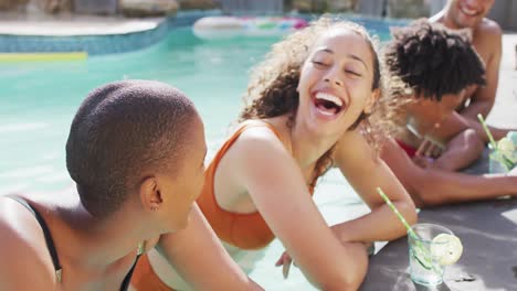 Two-diverse-female-friends-with-drinks-laughing-by-swimming-pool