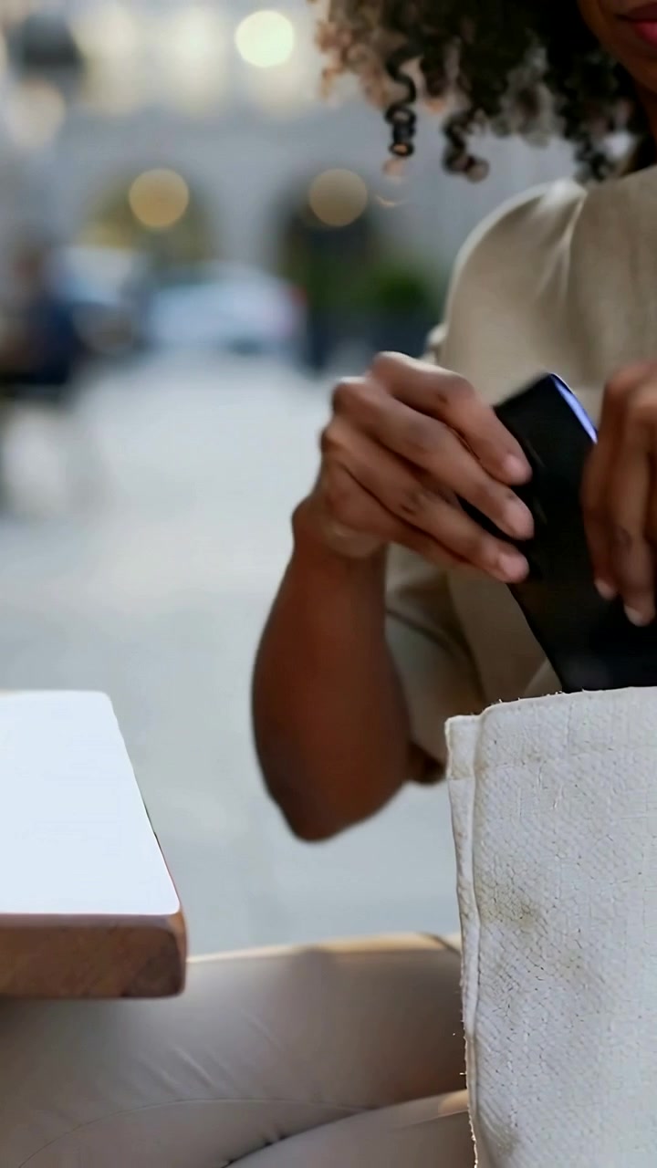 Vertical video: Picking up phone from cafe table, woman in tan top placing phone into tote to leave