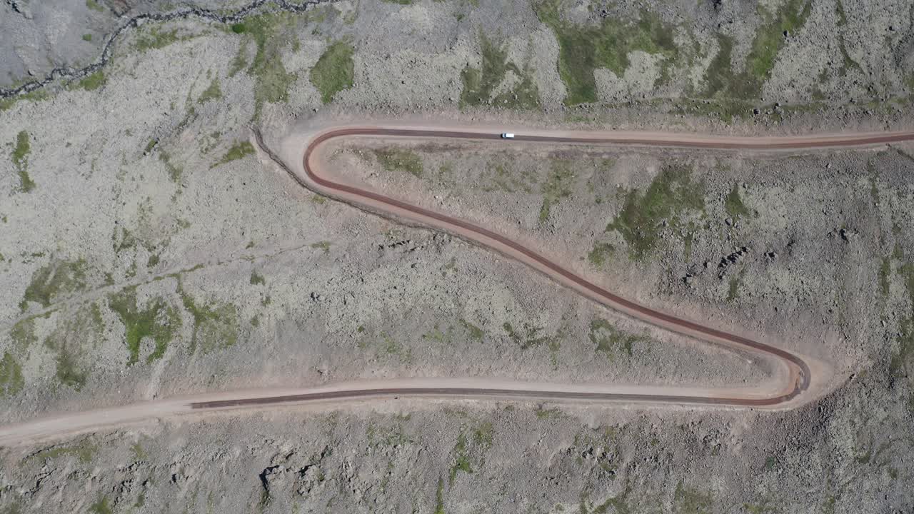 tomada aérea de arriba hacia abajo que muestra un coche en una carretera curva en las montañas de islandia, westfjords - calle rocosa con patrón
