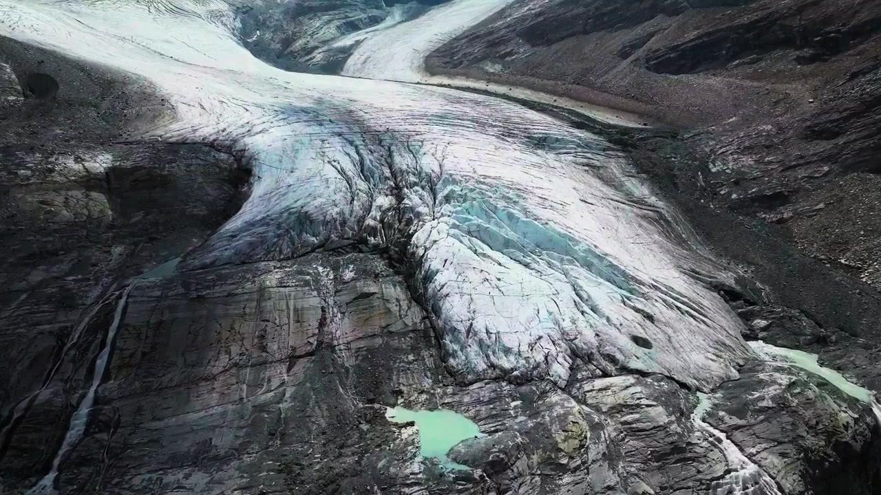 En slående filmisk luftoptagelse fra høj vinkel med sporing, der fanger alvorlig overfladesmeltning, smeltevandssøer og dybe sprækker på tværs af en tilbagetrækkende gletsjer i de schweiziske alper.