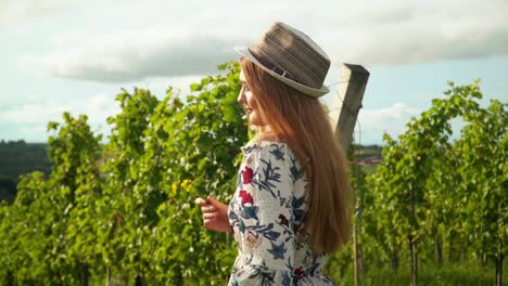 Stunning-HD-footage-of-a-Caucasian-girl-with-a-knitted-hat-and-red-lipstick-standing-in-a-vineyard,-illuminated-by-sunlight,-posing-and-smiling-for-teh-camera