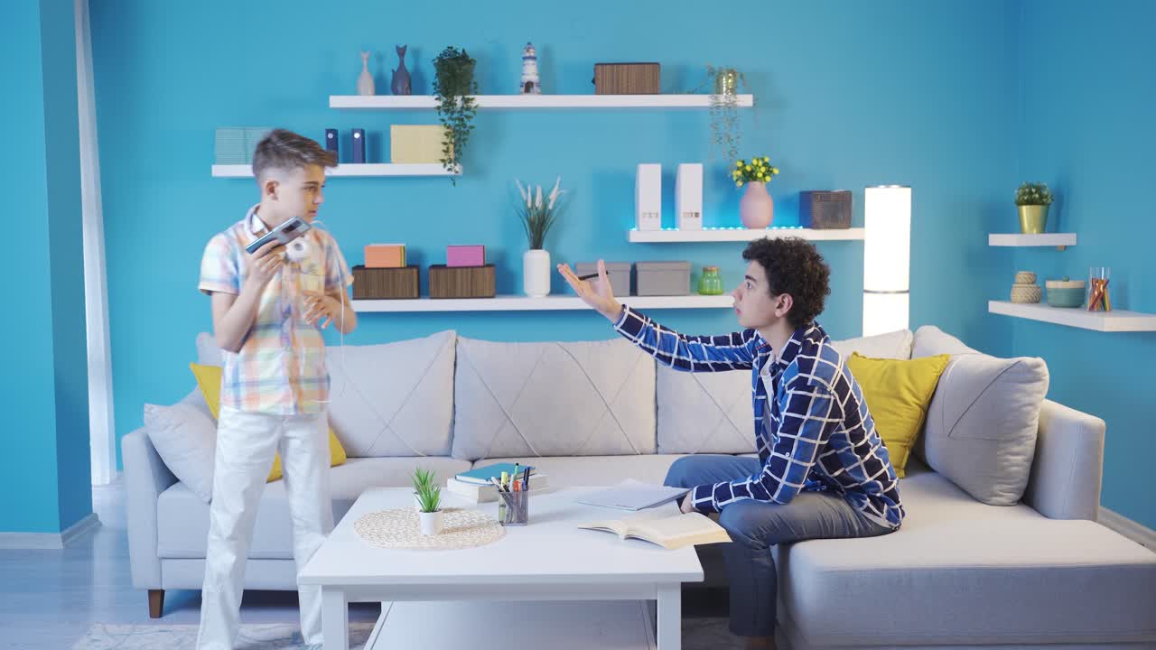 Little boy listening to loud music annoys his older brother who is studying.