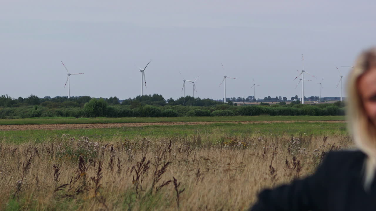Young businesswoman on the field. Camera raid on a young woman standing in a field, outdoor. Wind turbine or real estate techonology sale concept