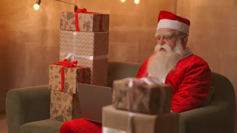 Videollamadas-De-Papá-Noel-Para-Llevar-Al-Niño-En-La-Computadora-Portátil,-Mantener-Presente,-Sentarse-En-La-Mesa-De-Casa.-La-Pandemia-Y-El-Aislamiento-Del-Santa-Felicita-A-Los-Niños-A-Distancia.-Imágenes-4k-De-Alta-Calidad