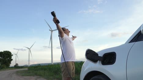 progressive man with his ev car and wind turbine as concept of renewable energy.