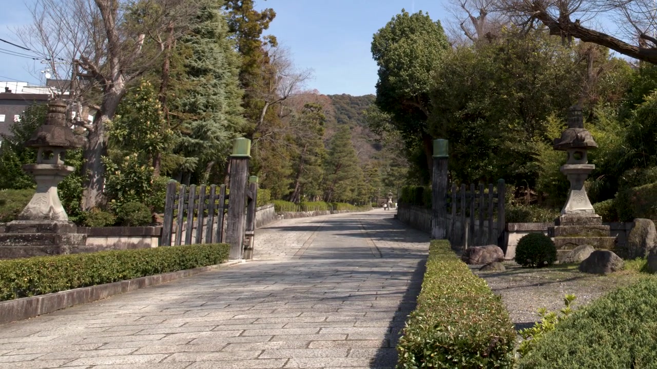 Inquadratura ampia statica di un sentiero lastricato in pietra attraverso un sereno giardino giapponese e un santuario.