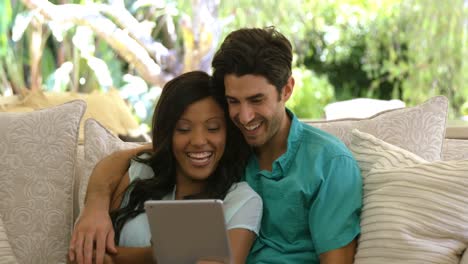 una pareja joven sentada en el sofá y usando una tableta digital en la sala de estar